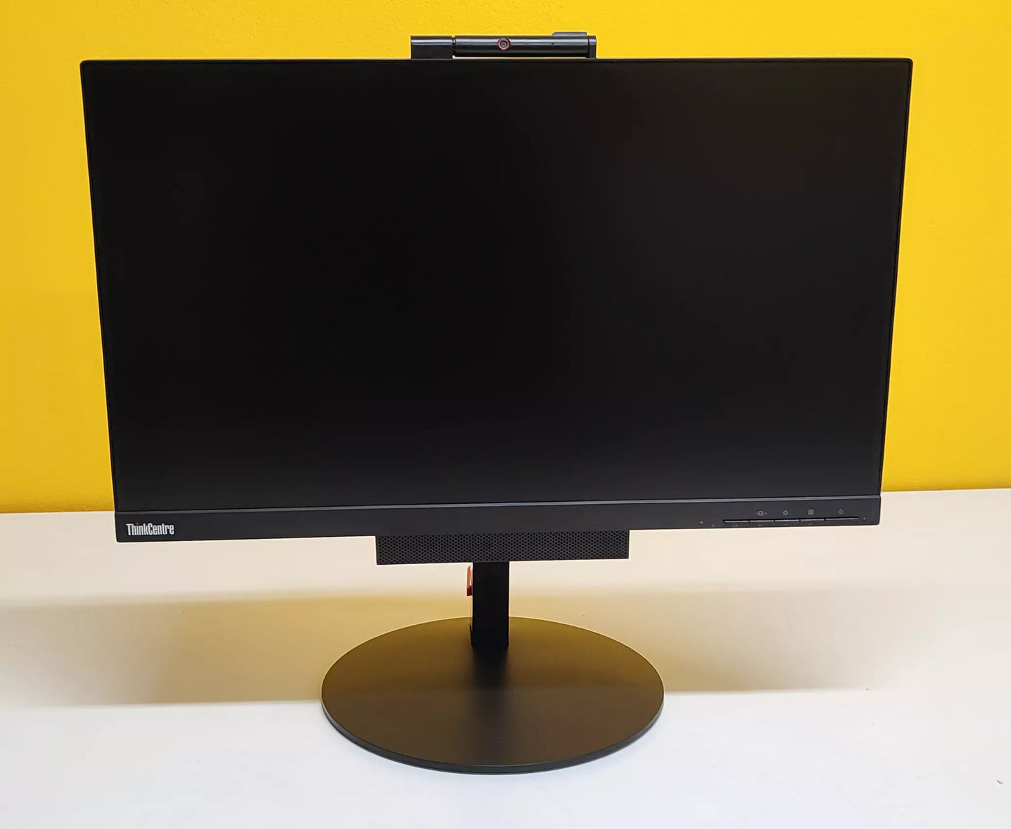 Lenovo ThinkCentre TIO24 All-in-One spento su sfondo giallo, con design elegante e base circolare stabile per scrivanie moderne.